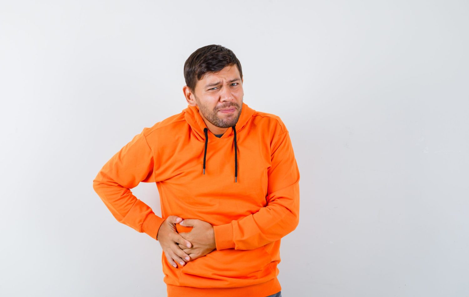 young male in orange hoodie suffering from abdominal pain and looking unwell , front view.