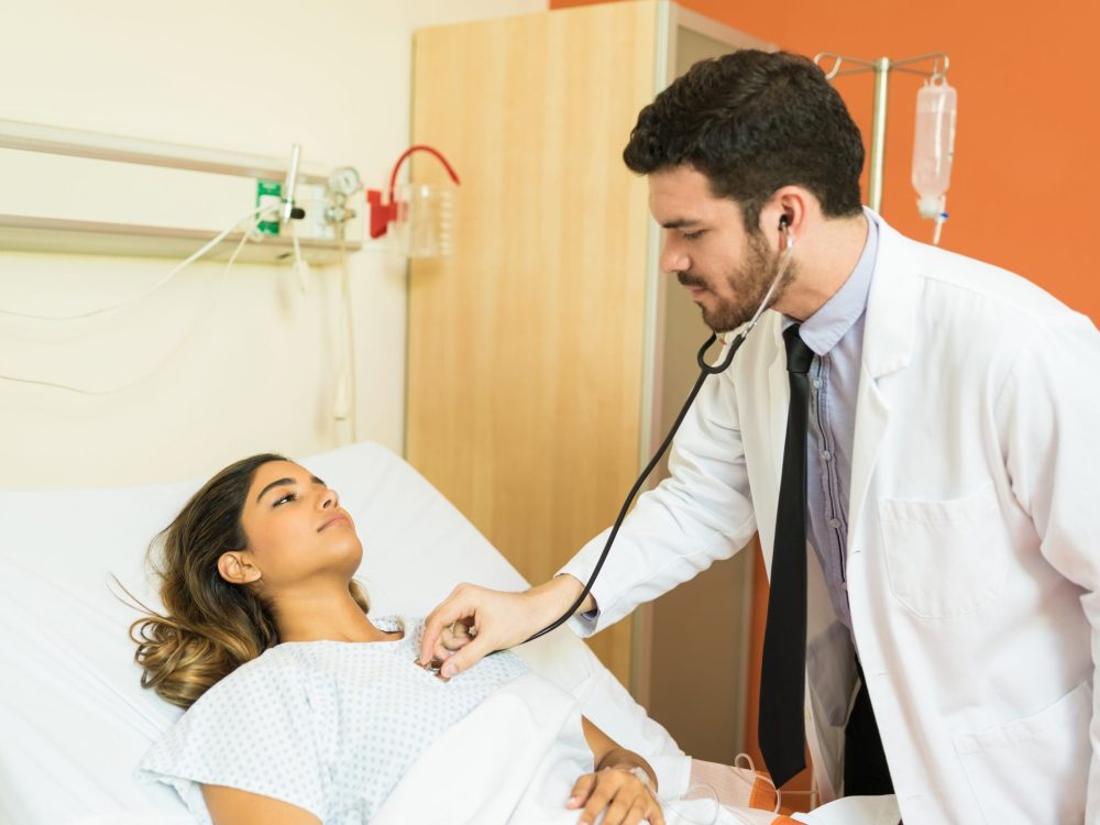 Hispanic male doctor examining patient with stethoscope at hospital