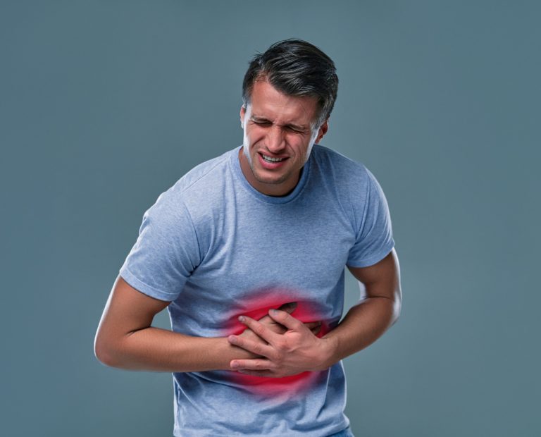 Man in white t-shirt holding his stomach due to stomachache